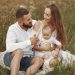 A joyful couple with their baby sitting on a blanket in a sunny meadow, embracing the beauty of summer.